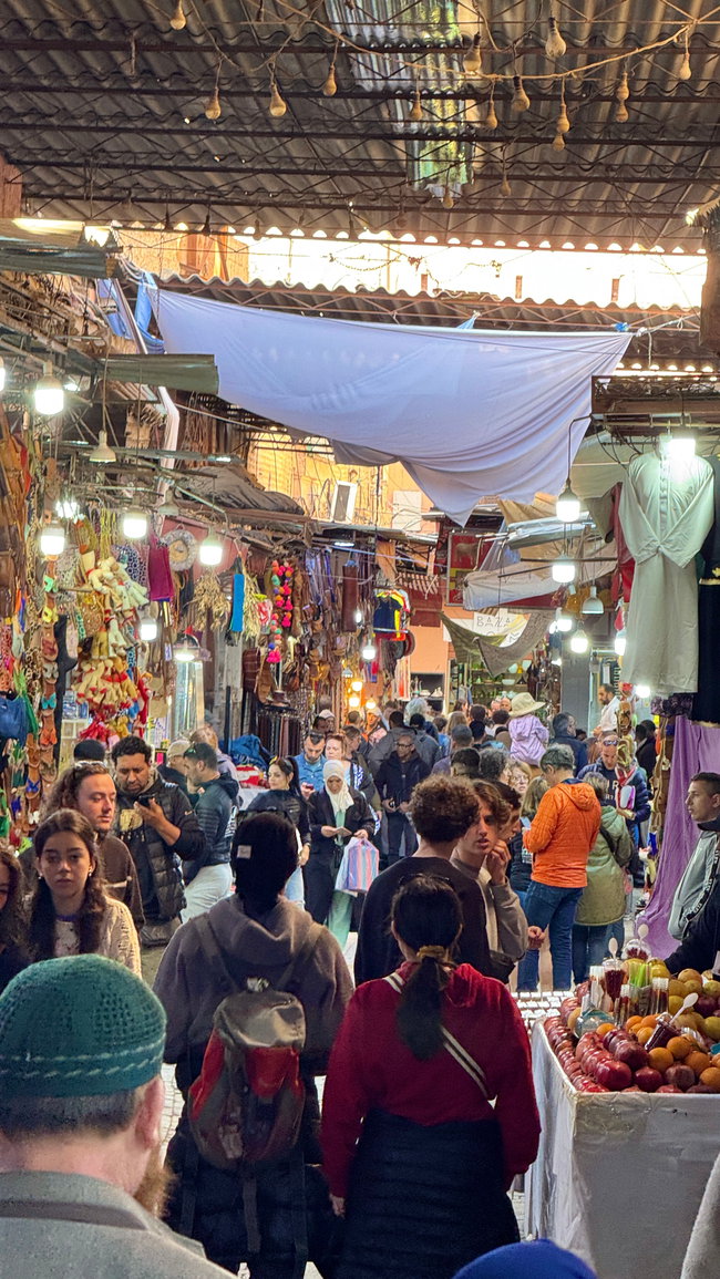 Voyage à moto au Maroc MM6 – Dans les ruelles étroites du marché Ruelle traditionnelle du souk de Marrakech bordée de petites boutiques et d’étals