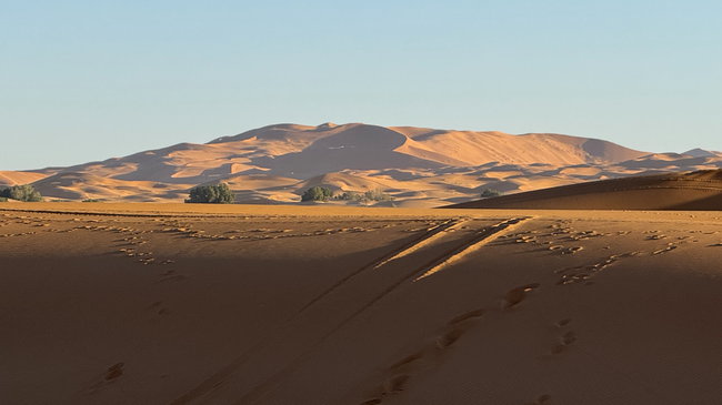 Voyage moto au Maroc MM8 – Les premières grandes dunes de sable du Sahara Premières grandes dunes de sable du Sahara à l'horizon, le long d'une route asphaltée dans le sud du Maroc