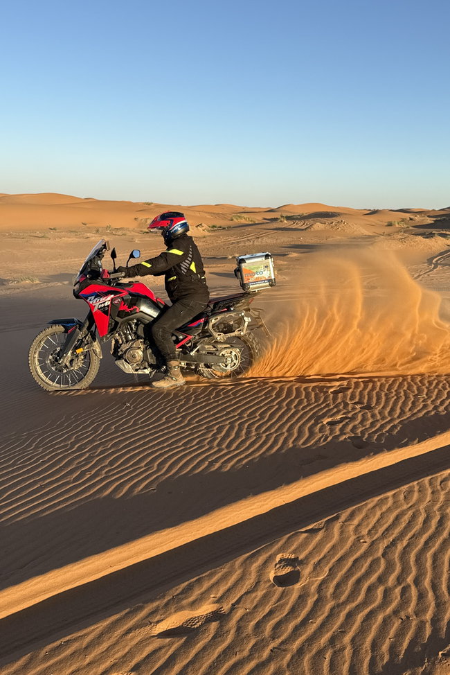 Moto et Sahara – Arrêt photo devant les dunes de sable Moto photographiée dans le paysage désertique du Maroc